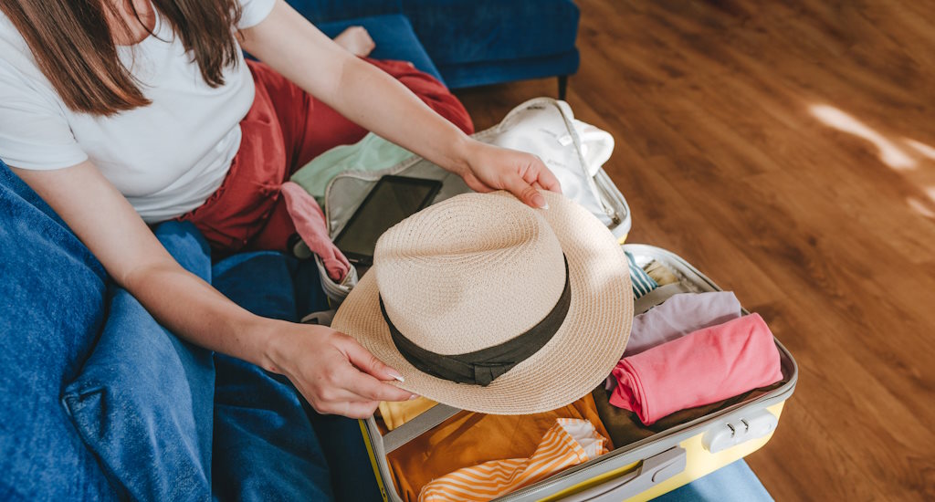 Packliste für Welnessurlaub mit Trolley und Frau mit Hut